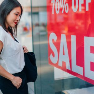 Beautiful young Asian woman looking at window display at retail store during sale.