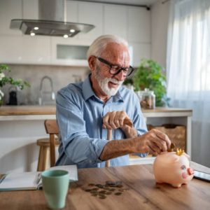 An elderly man carefully places coins into his piggybank, symbolizing wisdom and the importance of saving. His facial expression reflects peace and contentment, as he believes in long-term goals and the power of small, consistent contributions to financial security.