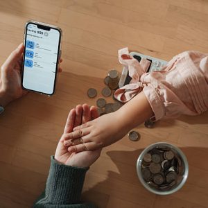 Mom teaching her daughter to understand the value of saving, showing her how to divide money into different categories for specific purposes, using a smartphone budgeting app to make the process fun and interactive. Together, they explore how to allocate money for saving, spending, and future goals, with colorful visuals and easy-to-follow charts on the screen
